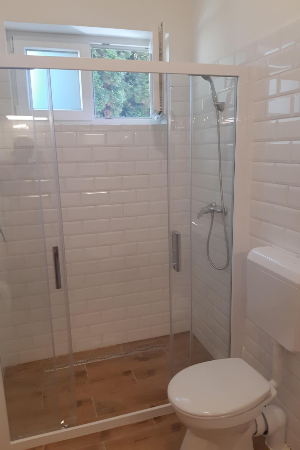 A bathroom with a glass-enclosed shower, a toilet, and white tiled walls.