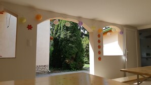 A room with a wooden table and benches, an arched doorway leading to a garden, and a ceiling light fixture.