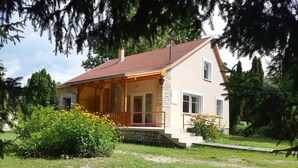 A two-story house with a red-tiled roof, stone foundation, and a wooden porch.