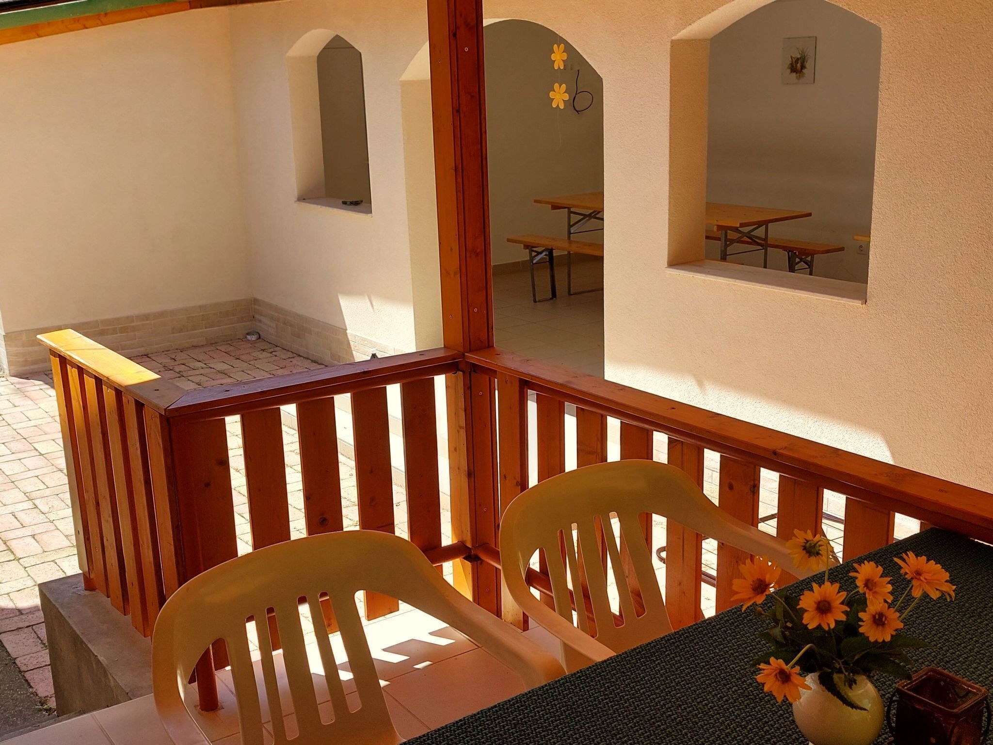 Ein Balkon mit Holzgeländern, zwei gelben Plastikstühlen und einem Tisch mit einem Blumenstrauß.