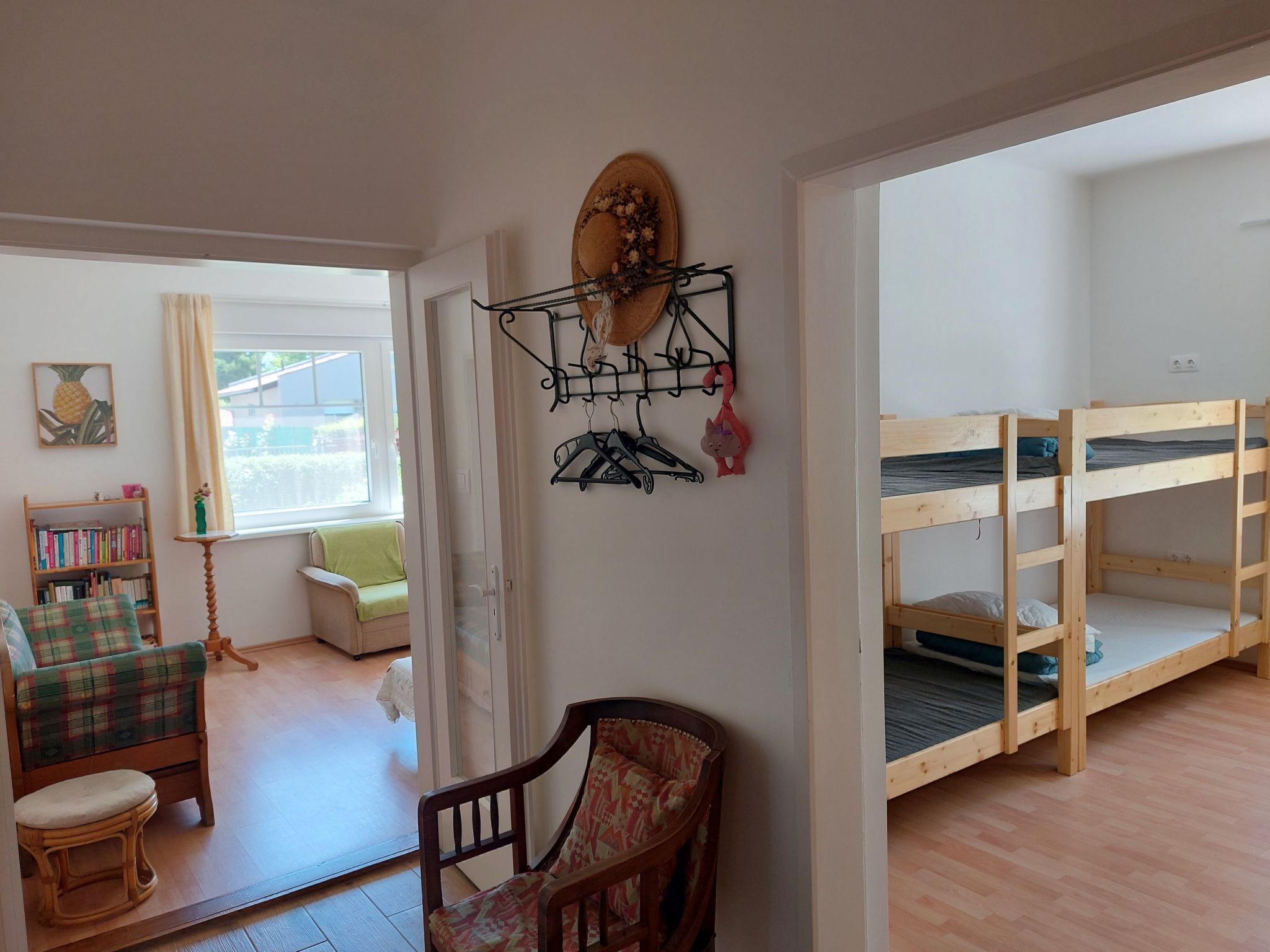 A room with bunk beds, a chair, a small table, a bookshelf, and a window with curtains.