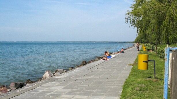 Un chemin pavé longe un plan d’eau, où des personnes se détendent et se promènent.