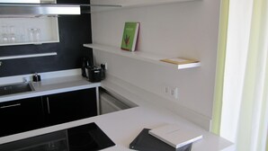 A modern kitchen with white countertops, a black stove, and a coffee maker. There are shelves with a book and a small box. - Penthouse mit Donaublick by Interhome (Budapest)