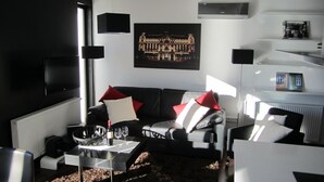 A modern living room with a black leather sofa, a coffee table, and a flat-screen TV. There is a framed picture on the wall and a radiator under the window. - Penthouse mit Donaublick by Interhome (Budapest)