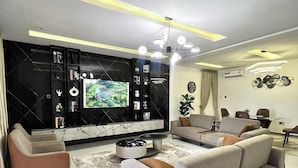 A modern living room with a large flat-screen TV, a sofa, a coffee table, and a dining area with a table and chairs.