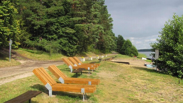 A row of wooden benches along a dirt path in a wooded area with a lake in the background. - Holiday Home, Nowa Kaletka (Purda)