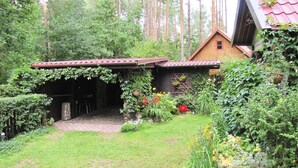 A rustic wooden cabin with a red-tiled roof, surrounded by lush greenery and tall trees. - Holiday Home, Nowa Kaletka (Purda)