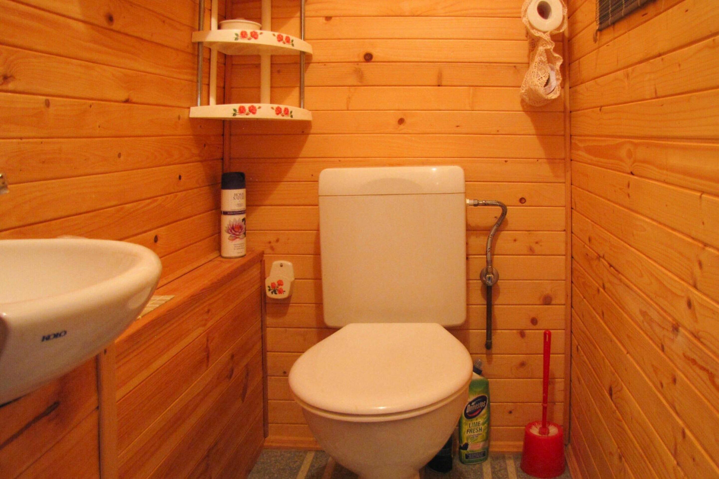 Ein kleines Badezimmer aus Holz mit Toilette, Waschbecken und Ablage für Pflegeprodukte.