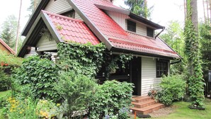 A two-story house with a steeply pitched roof, surrounded by lush greenery and trees. - Holiday Home, Nowa Kaletka (Purda)