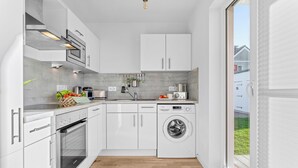 Une cuisine moderne avec des meubles blancs, un four encastré, un lave-vaisselle et un lave-linge.