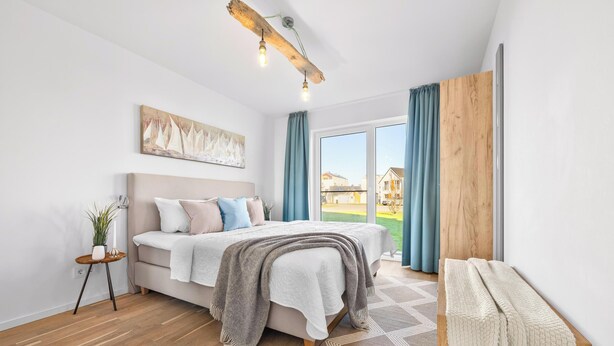 Une chambre à coucher avec un lit, une table de chevet, une fenêtre avec des rideaux et un tableau accroché au mur.
