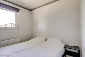 Et simpelt soveværelse med en enkeltseng, et natbord, et vindue med skodder og en radiator.