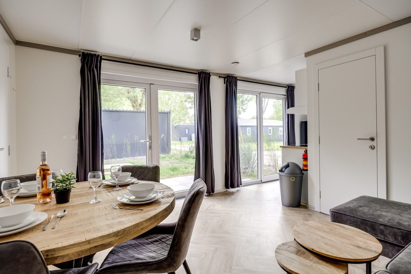A modern dining area with a round wooden table, dark curtains, and a view of the outdoors.