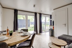 Et moderne spiseområde med et rundt træbord, mørke gardiner og udsigt til det fri.