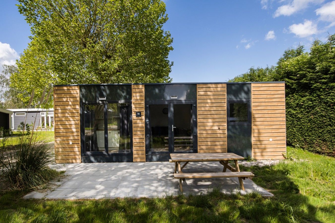 Een modern gebouw met een houten gevel, grote glazen deuren en een picknicktafel ervoor.