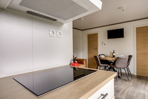 Una cocina moderna con encimera negra, un extintor rojo y un comedor con mesa y sillas de madera.