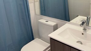 Un bagno con un water bianco, un lavabo con uno specchio e una tenda blu per la doccia.