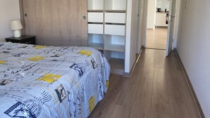 Una camera da letto con un letto, un comodino, una lampada, un'armadio in legno e vista sulla cucina.