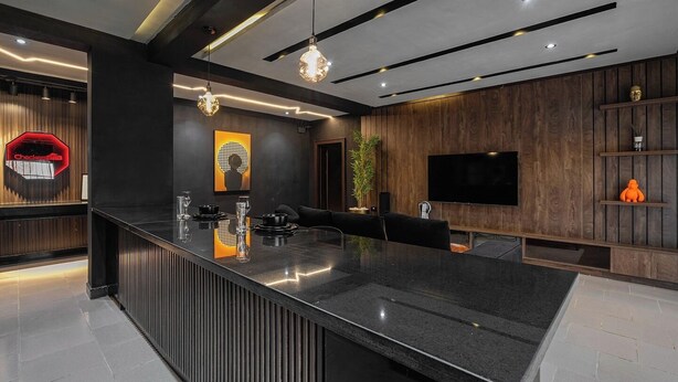 Una cocina moderna con una isla central, paneles de madera oscura y un televisor de pantalla plana montado en la pared.