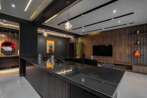 A modern kitchen with a central island, dark wood paneling, and a flat-screen TV mounted on the wall. - Oputa Jay Apartment (Abuja)