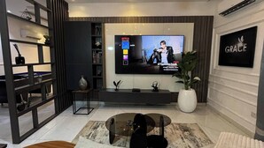 Una sala de estar moderna con una mesa de centro de vidrio, un televisor montado en la pared y una lámpara de araña decorativa.