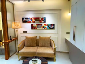 Una sala moderna con un sofá color beige, dos almohadones decorativos, una lámpara de pie y arte abstracto en la pared.