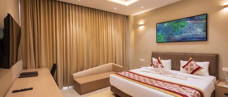 A hotel room with a bed, a desk, a television, and a painting on the wall.