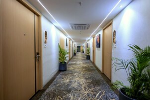 Un pasillo de hotel con puertas, plantas en macetas y una alfombra estampada.