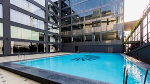 A swimming pool with a geometric design, surrounded by a building with large windows and a tiled floor. - Saaz Hotel, Club & Convention Centre (Indore)
