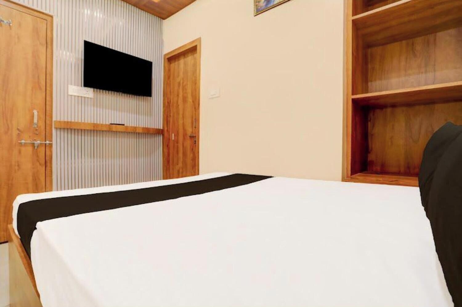 A bedroom with a bed, wooden wardrobe, and a mounted television.
