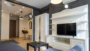 A modern living room with a sofa, a coffee table, a TV on a white cabinet, and a clock on the wall. - the business class suit karkoy (Istanbul)