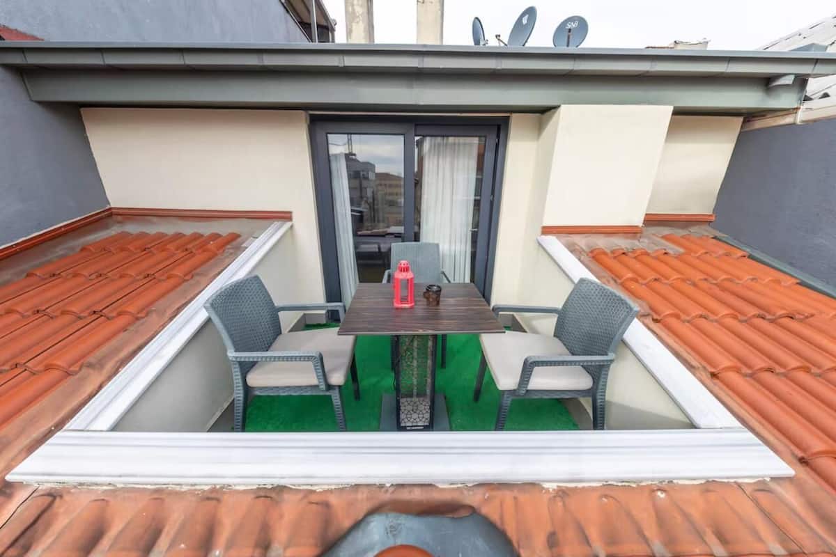 A rooftop terrace with a table and chairs, a sliding glass door, and a view of the cityscape.