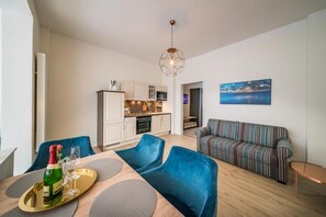 A modern living room with a dining area, a striped sofa, and a kitchen in the background. - Villa Sofia - Nordlicht: Comfortable vacation apartment on Borkum near the sandy beach (Borkum)