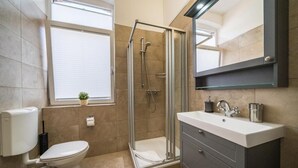 A modern bathroom with a toilet, a glass-enclosed shower, a sink with a mirror, and a window with blinds. - Villa Sofia on Borkum - Stylish vacation apartment in a central location (Borkum)