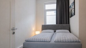 A bedroom with a bed, a nightstand, a window with curtains, and a painting on the wall. - Villa Sofia on Borkum - Stylish vacation apartment in a central location (Borkum)