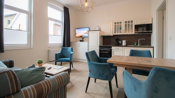 A compact living space with a kitchenette, a sofa, two chairs, a wooden dining table, and a hanging light fixture. - Villa Sofia on Borkum - Stylish vacation apartment in a central location (Borkum)