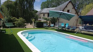 Ein Swimmingpool mit Rasen, Liegestühlen und einem Haus im Hintergrund.