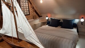 Ein Schlafzimmer mit einem Modell eines Segelboots, einem Holzkopfende, zwei Nachttischlampen und einer gerahmten Sammlung von Postkarten an der Wand.