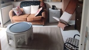 Ein gemütliches Schlafzimmer mit Dachschräge, ausgestattet mit einer braunen Ledersofa, einem kleinen runden Tisch und einem weißen Sessel. Ein gerahmtes Poster und eine Karte zieren die Backsteinwand.