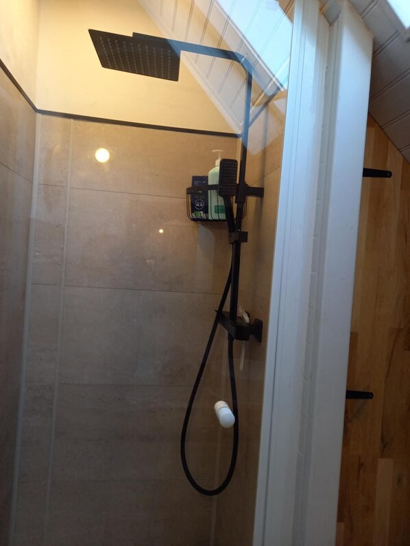 Een douche met een handdouche, een handscrubber en een fles shampoo.