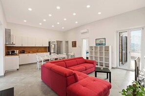Eine moderne Wohnung mit einem roten Ecksofa, einem Essbereich, einer Küche und einem Balkon mit Blick auf die Stadt.