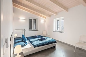 Ein Schlafzimmer mit einem Bett, zwei Nachttischlampen, einem Sessel und zwei Fenstern.