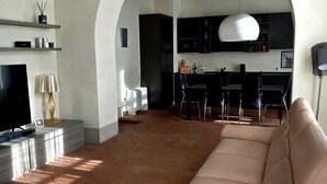 Een woonkamer met een bank, televisie en een keuken die zichtbaar is door een boog.