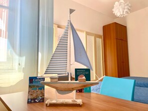 Ein Modellsegelschiff auf einem Holztisch, daneben ein Buch mit dem Titel "PIRANDELLO" und im Hintergrund ein blauer Stuhl.