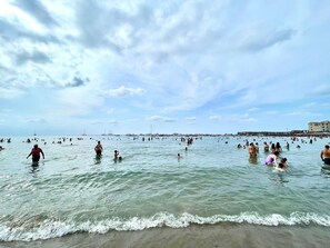 En fullsatt strand med folk som badar och promenerar i vattnet.