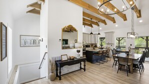 Uma cozinha espaçosa com vigas de madeira, sala de jantar com uma mesa grande e cadeiras, e vista para o exterior.