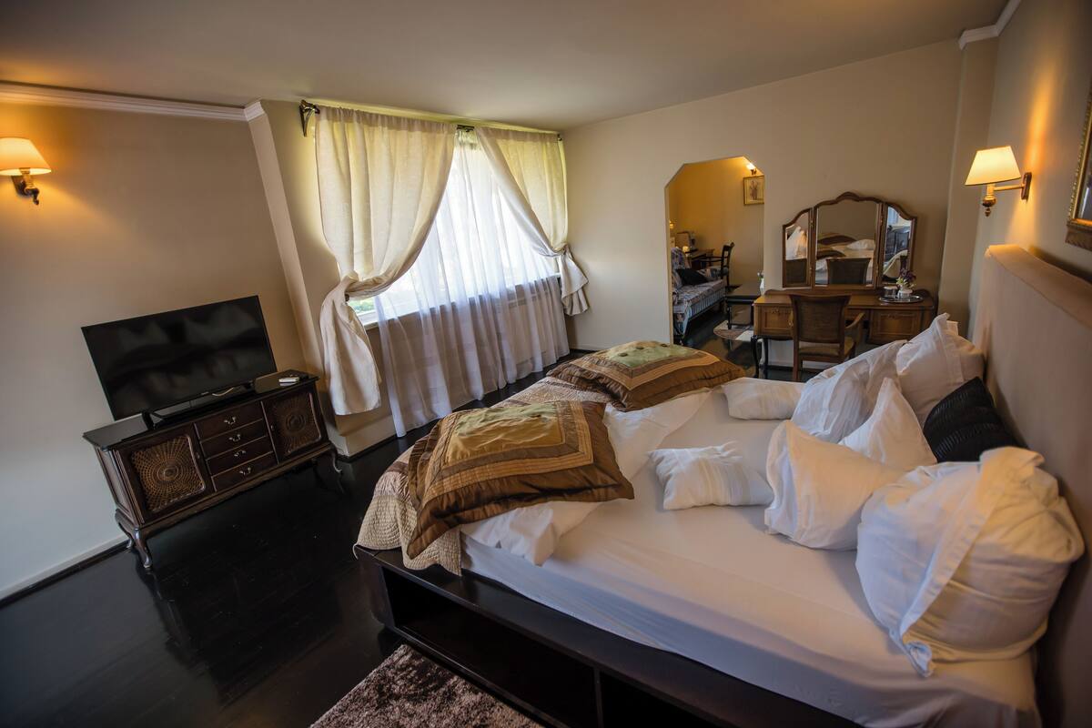 Una habitación de hotel con cama, televisión, escritorio y silla, y ventana con cortinas.