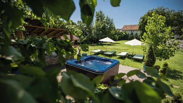 Ein Whirlpool in einem Garten mit einer Pergola, einem Rasen und einem Gebäude im Hintergrund.