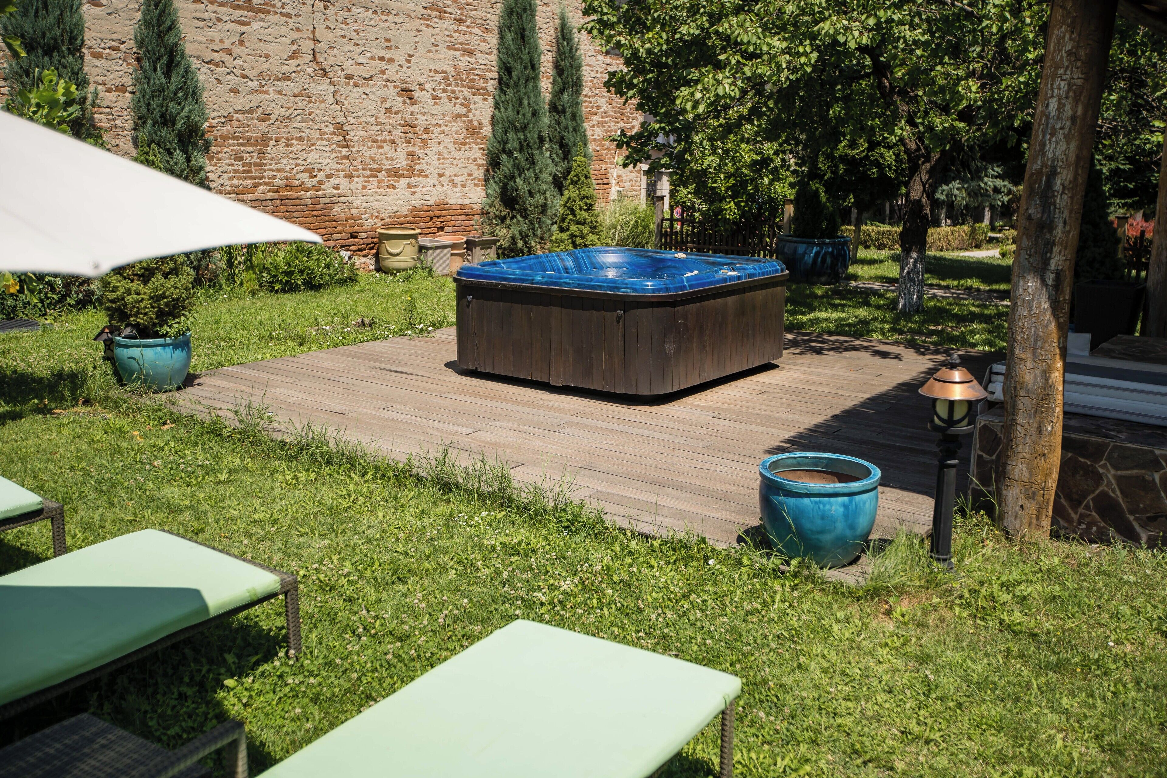 Un jacuzzi en una terraza de madera, rodeado de vegetación y un muro de ladrillo.