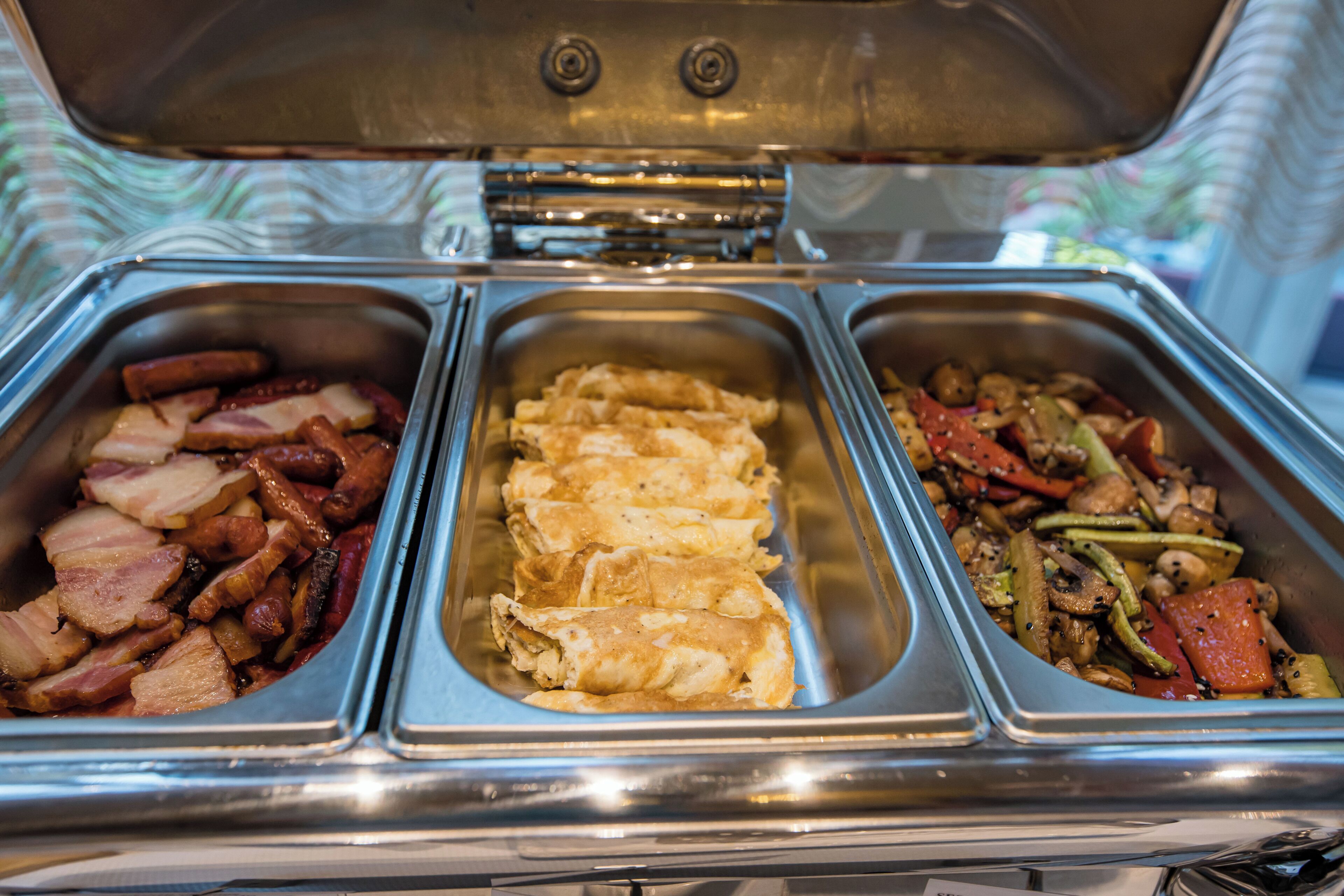 A buffet with three food sections: one with sliced meats, one with rolled items, and one with stir-fried vegetables.